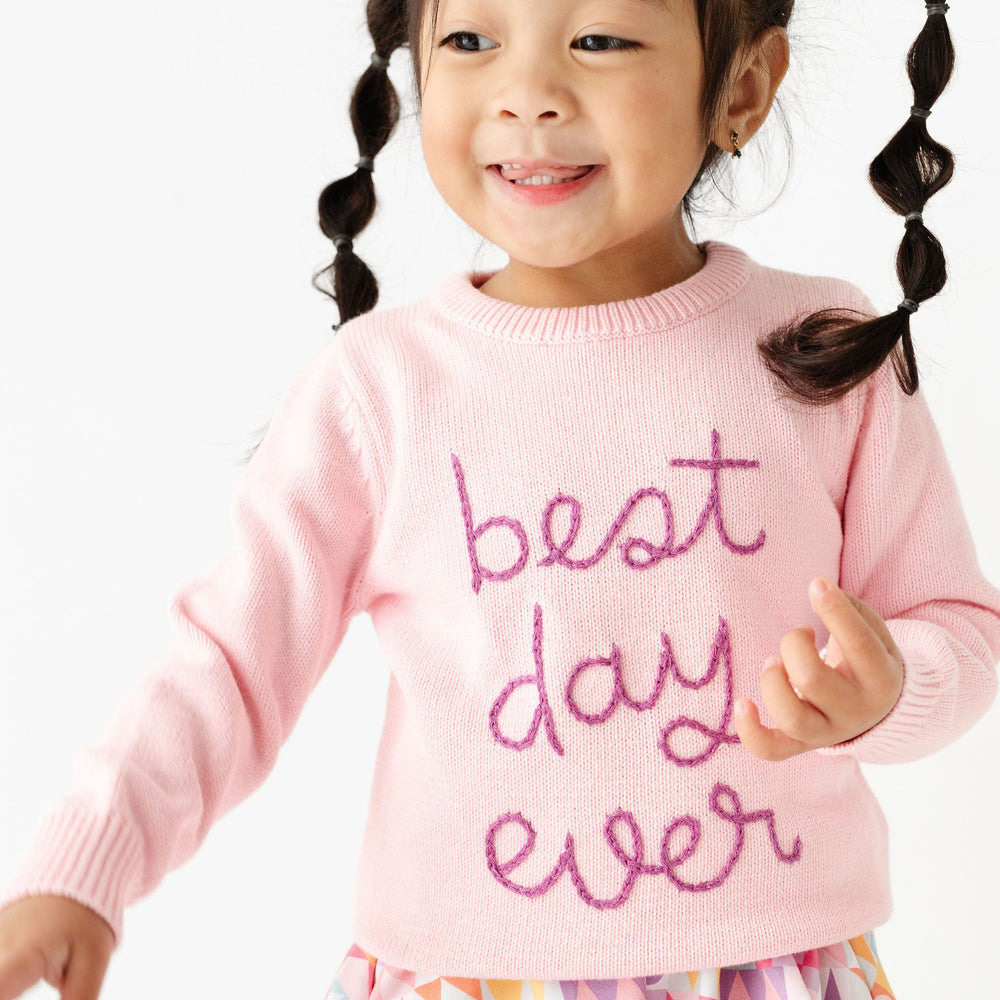 little girl wearing pink sweater with embroidered "best day ever" on front over disney inspired twirl dress