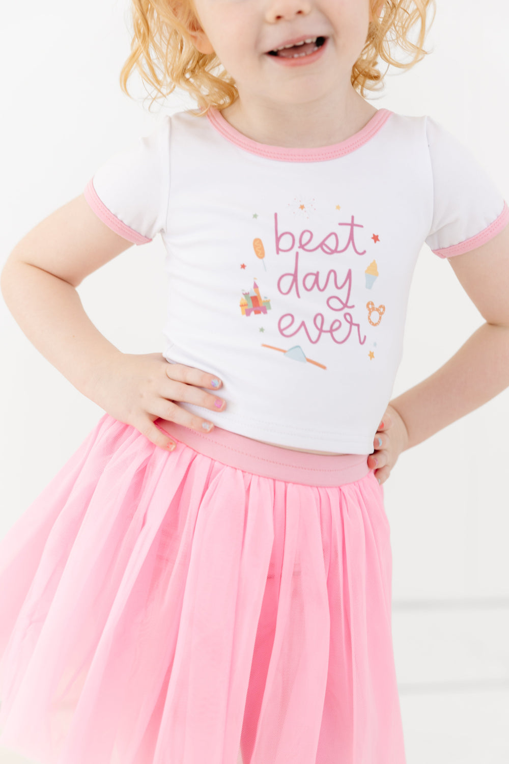 little girl in white magical top with light pink binding and "best day ever" print paired with pink tutu skirt for theme park days
