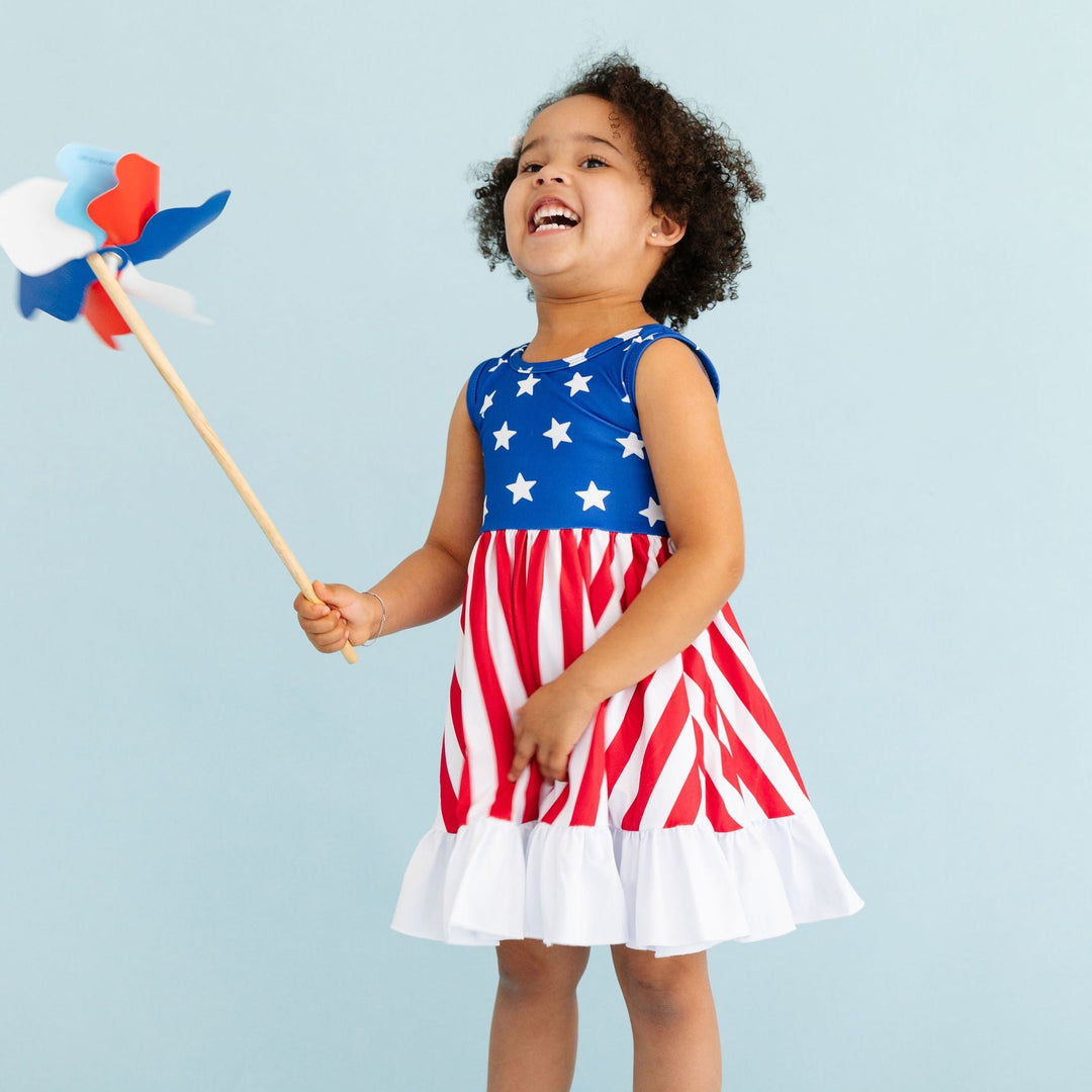 smiling little girl in american flag inspired dress holding red, white and blue pinwheel 