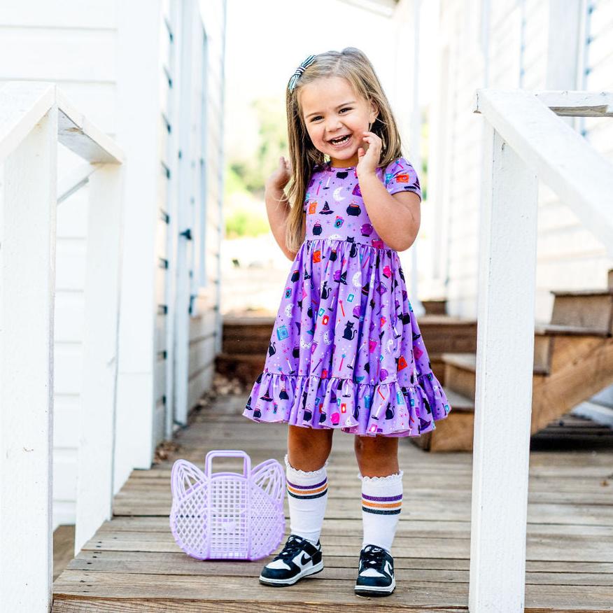 little girl wearing purple witch print dress and matching sparkle stripe knee highs for halloween