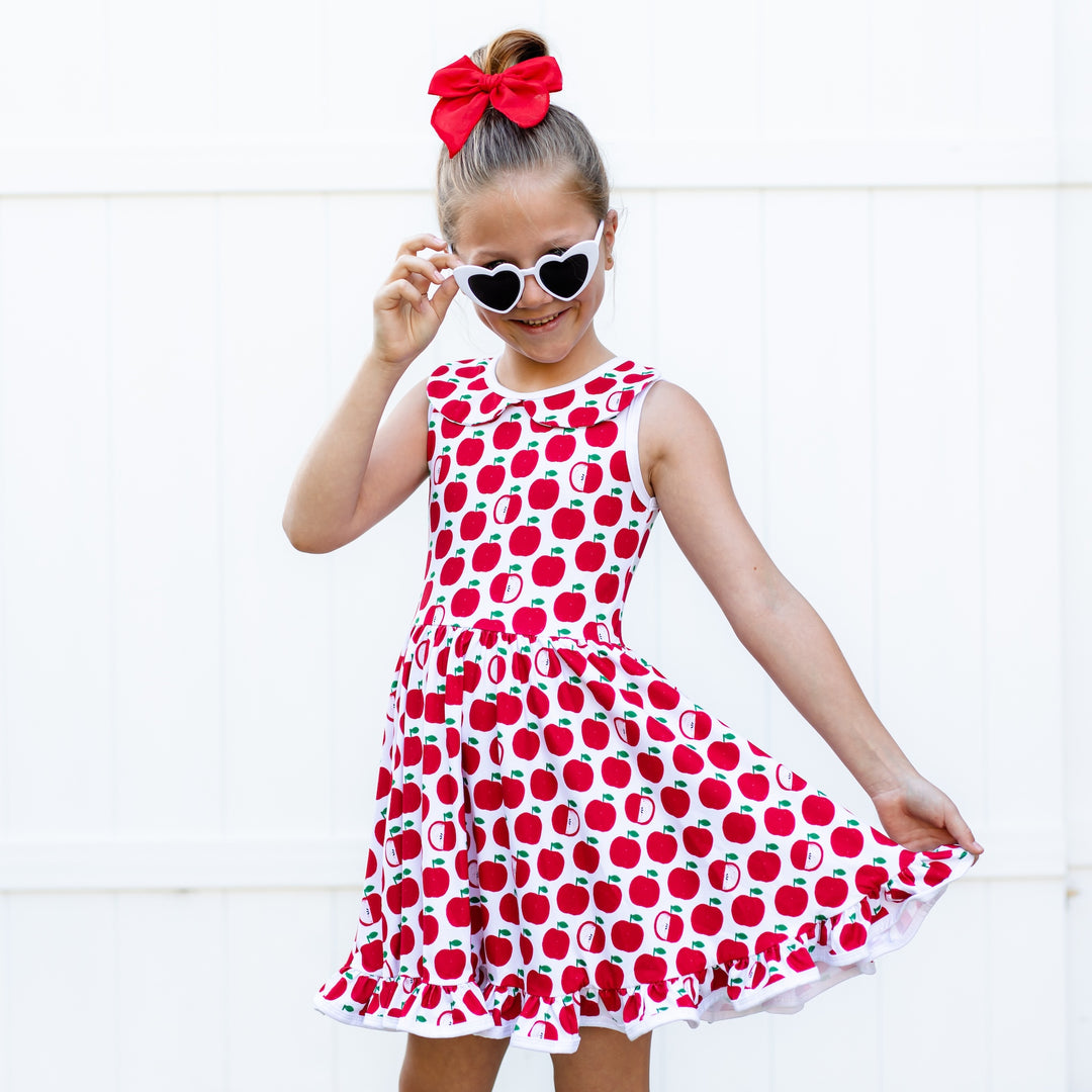little girl wearing apple print summer dress and white heart shaped sunglasses