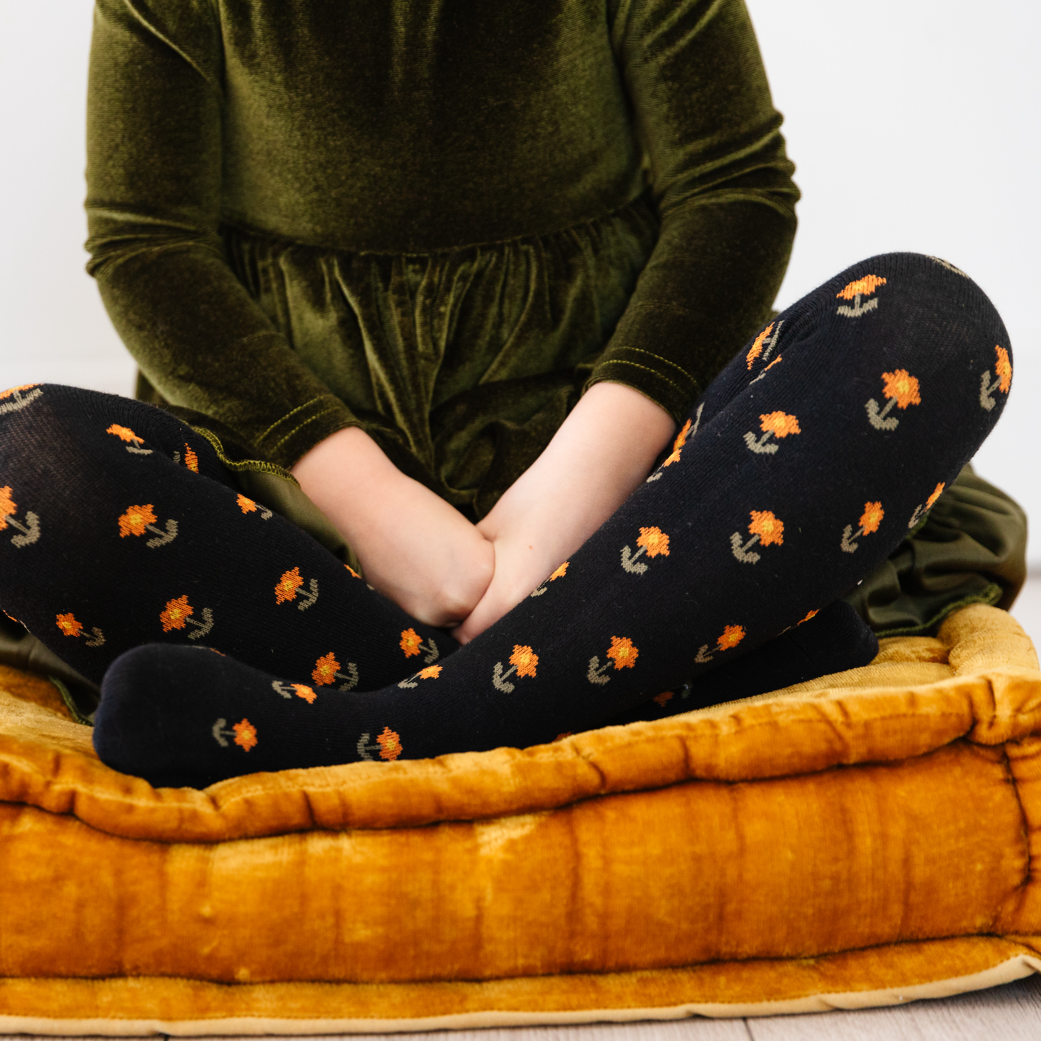 girl sitting with black tights with orange and yellow flowers on them and green velvet dress