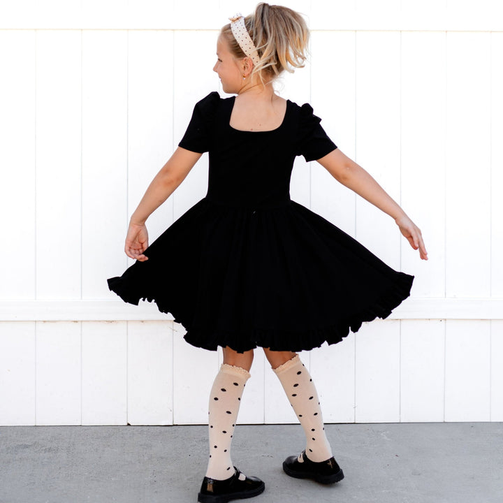 girl twirling in black square neck dress