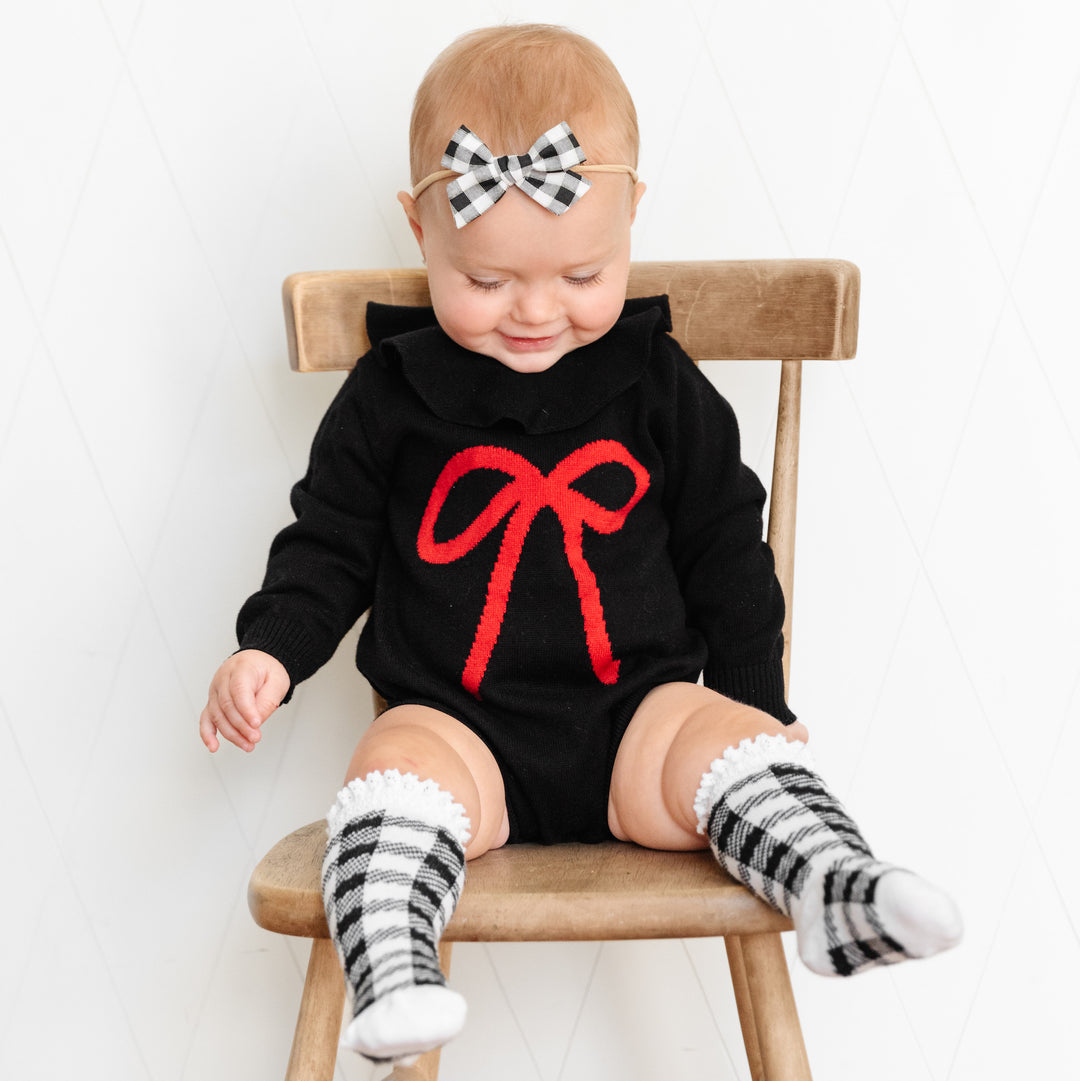baby girl sitting on chair wearing black and red bow sweater romper for christmas