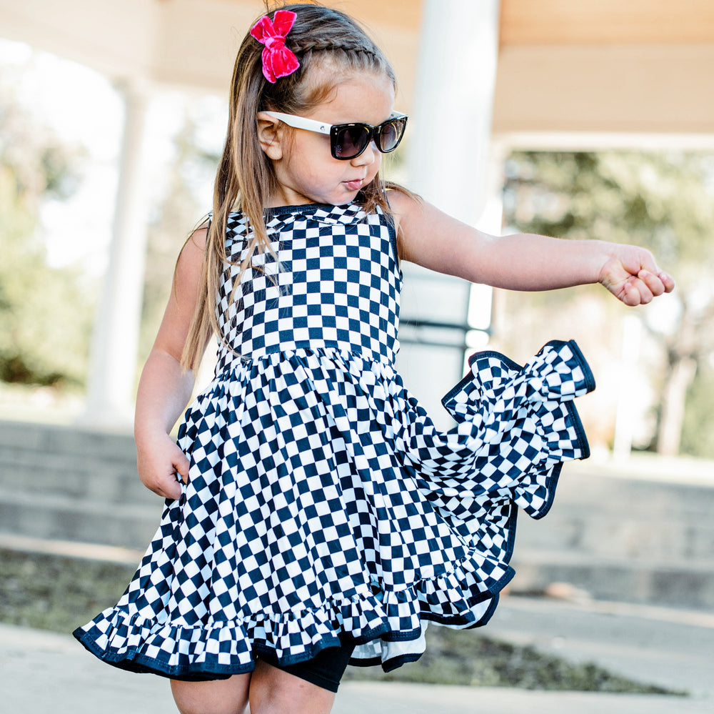 little girl wearing black and white checkered twirl dress and hot pink velvet hair bow