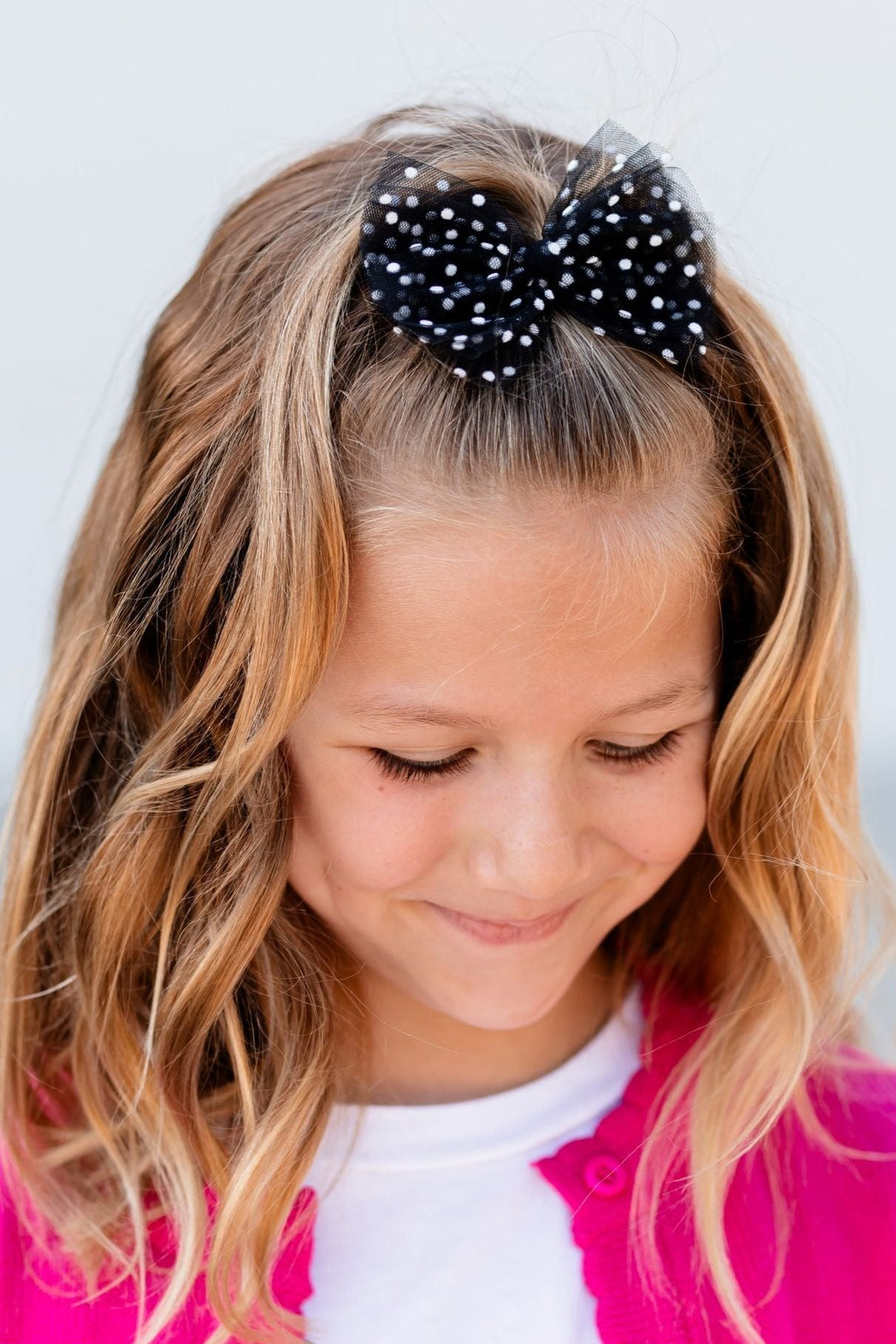 young girl wearing hot pink sweater with black and white dot sheer hair bow