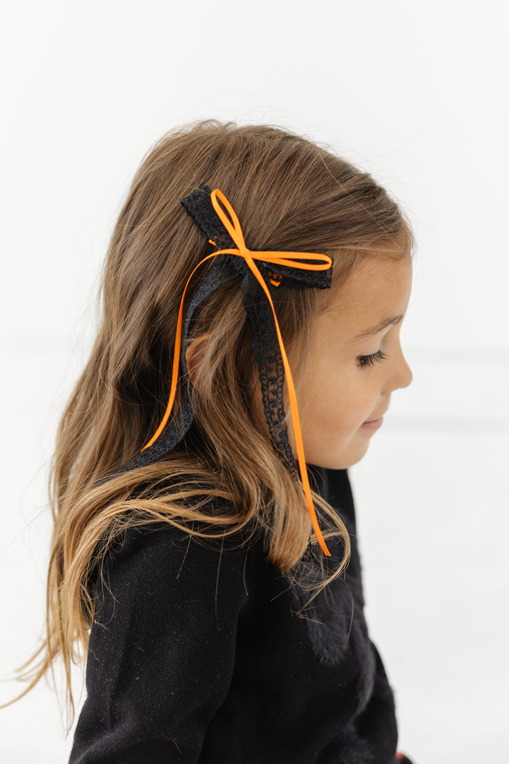 little girl in long black lace hair bow with orange ribbon accent bow on clip