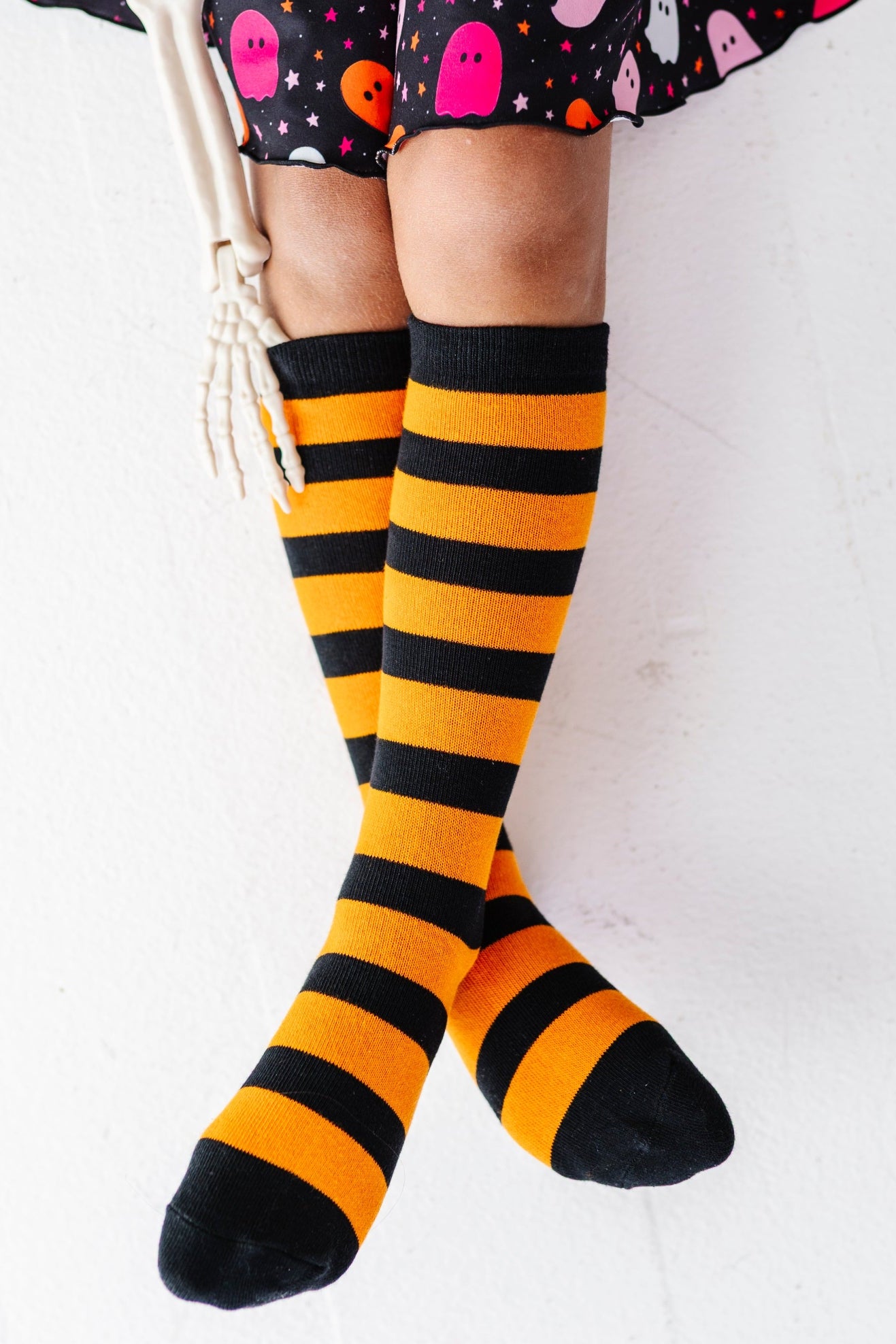 girl holding skeleton hand wearing black and orange horizontal striped knee socks paired with coordinating ghost print dress