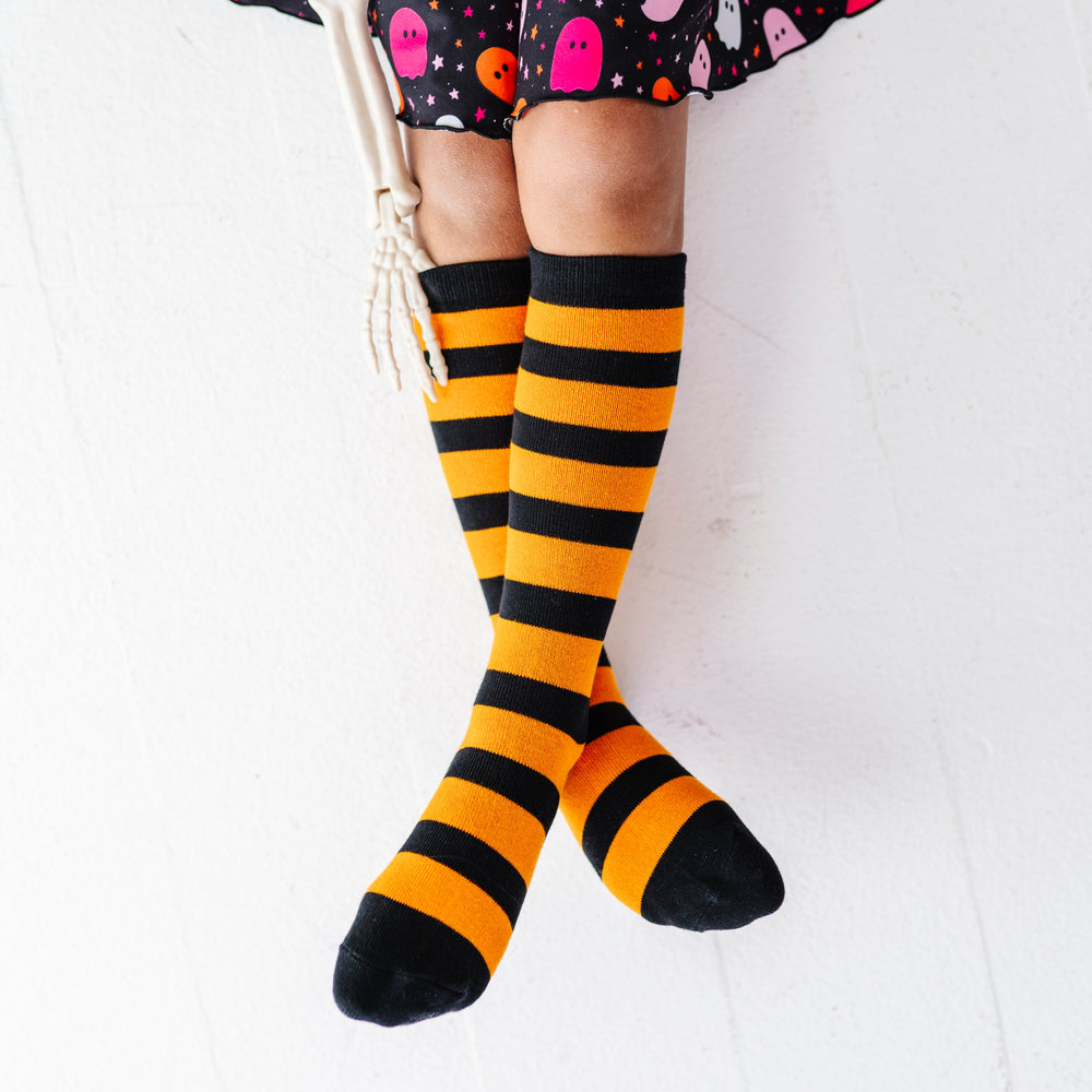 girl holding skeleton hand wearing black and orange horizontal striped knee socks paired with coordinating ghost print dress