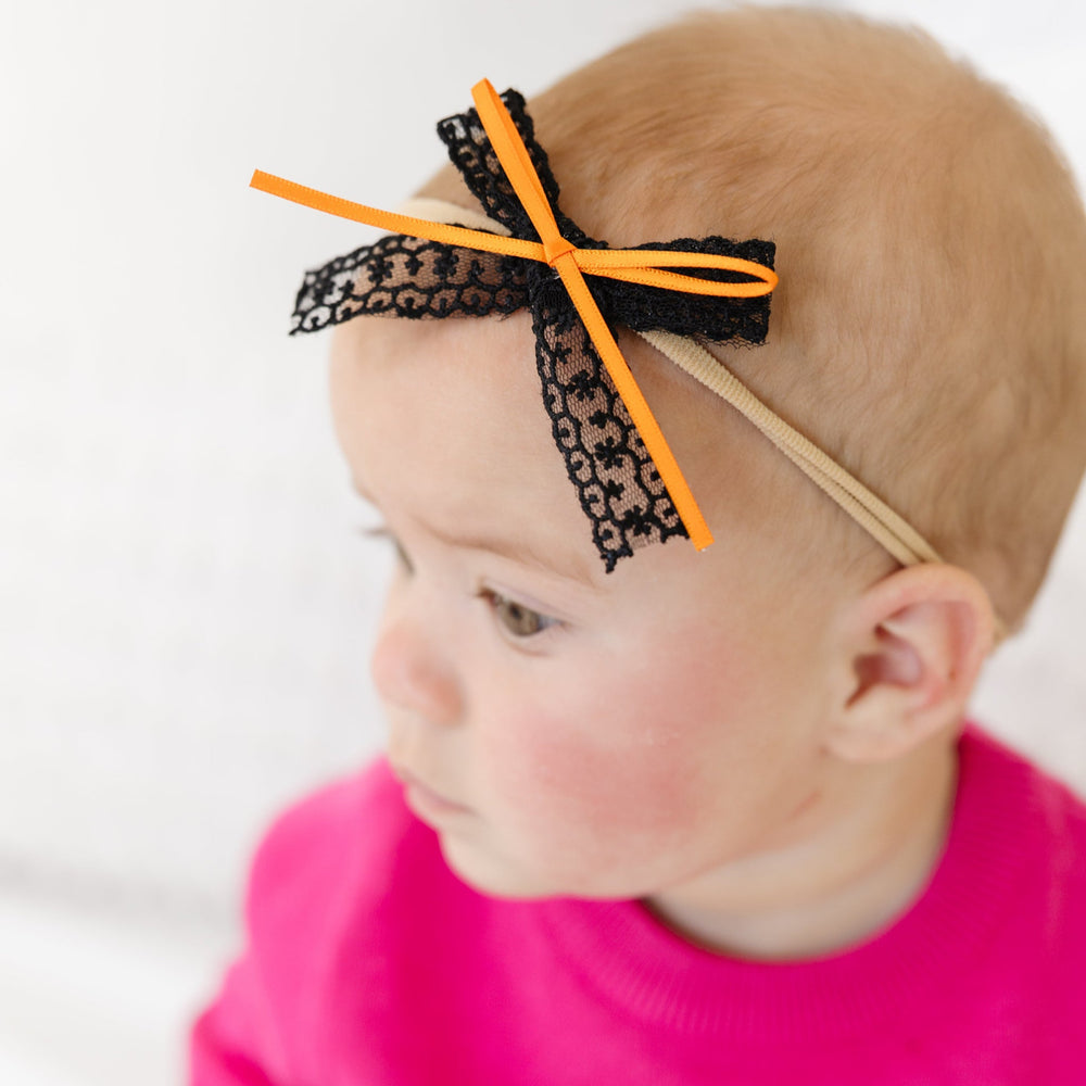 baby girl in bright pink sweater with ghost design and black lace bow on stretchy nylon with orange ribbon detail for Halloween