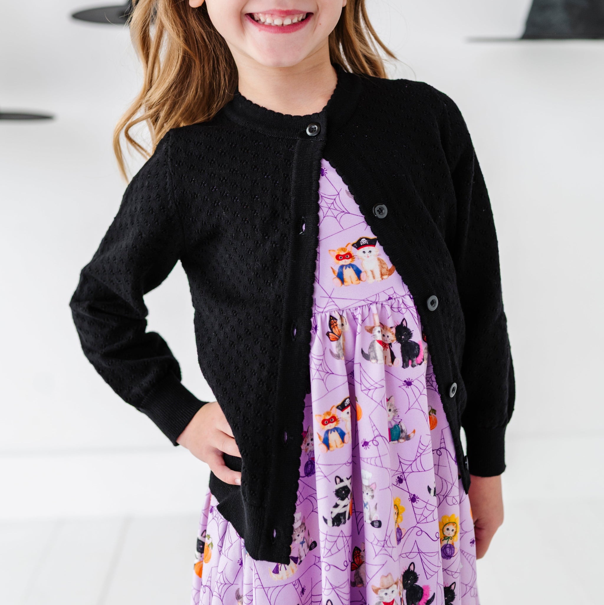 closeup of little girl wearing purple Halloween kitten twirl dress paired with black open knit pointelle cardigan with buttons