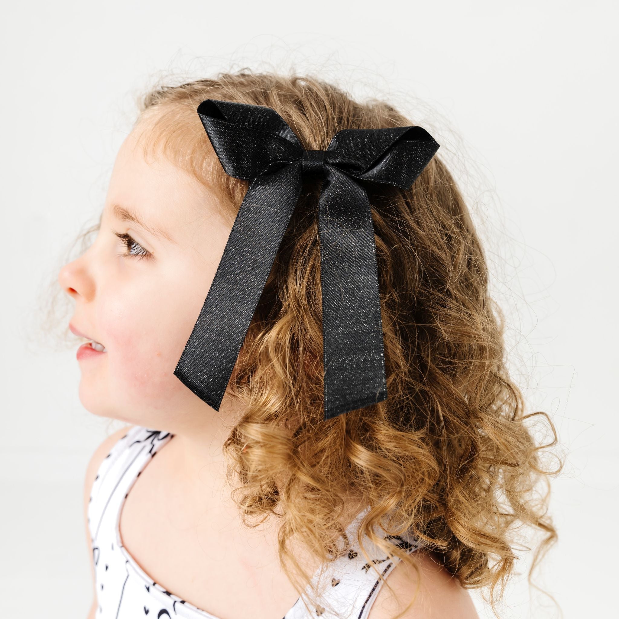 little girl wearing black shimmer ribbon bow on clip paired with monochrome bow print dress for summer