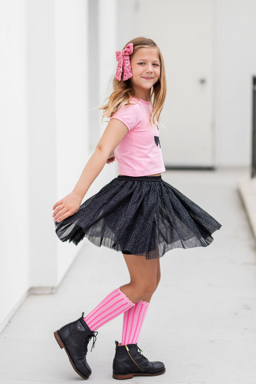 little girl twirling in sparkly black tulle skort with attached shorts and pink knee socks, top and sequin bow for pink Halloween