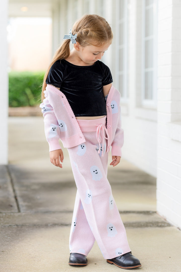 little girl in light pink cardigan with all over ghost print and matching sweater pants paired with black velvet top and black and white striped pigtail bows 