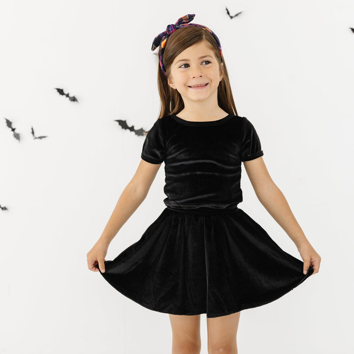 little girl in black velvet fitted top and skort set paired with black lettuce trim midi socks and October plaid headband