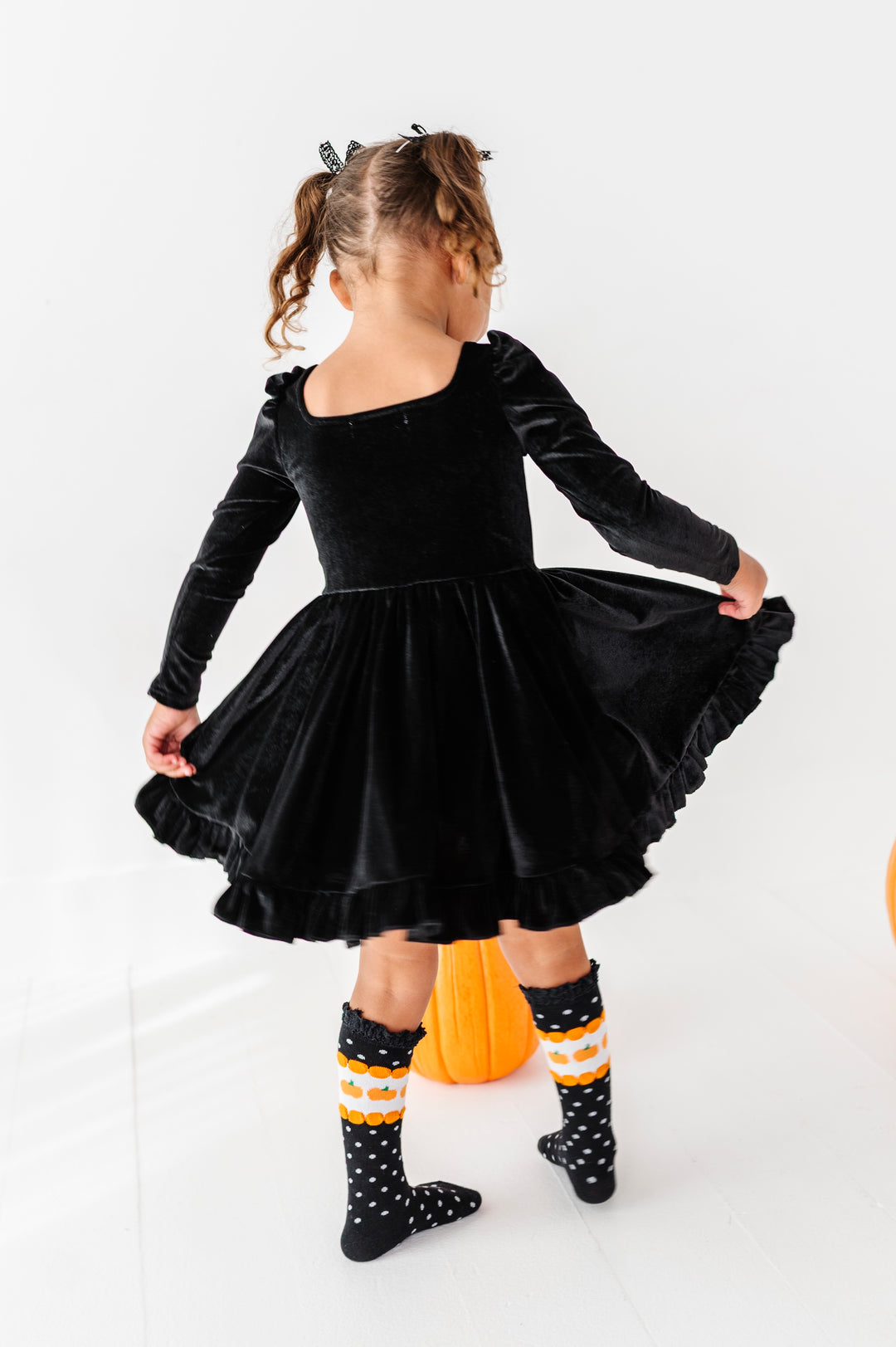 little girl twirling in long sleeve black velvet dress with halloween themed knee high socks