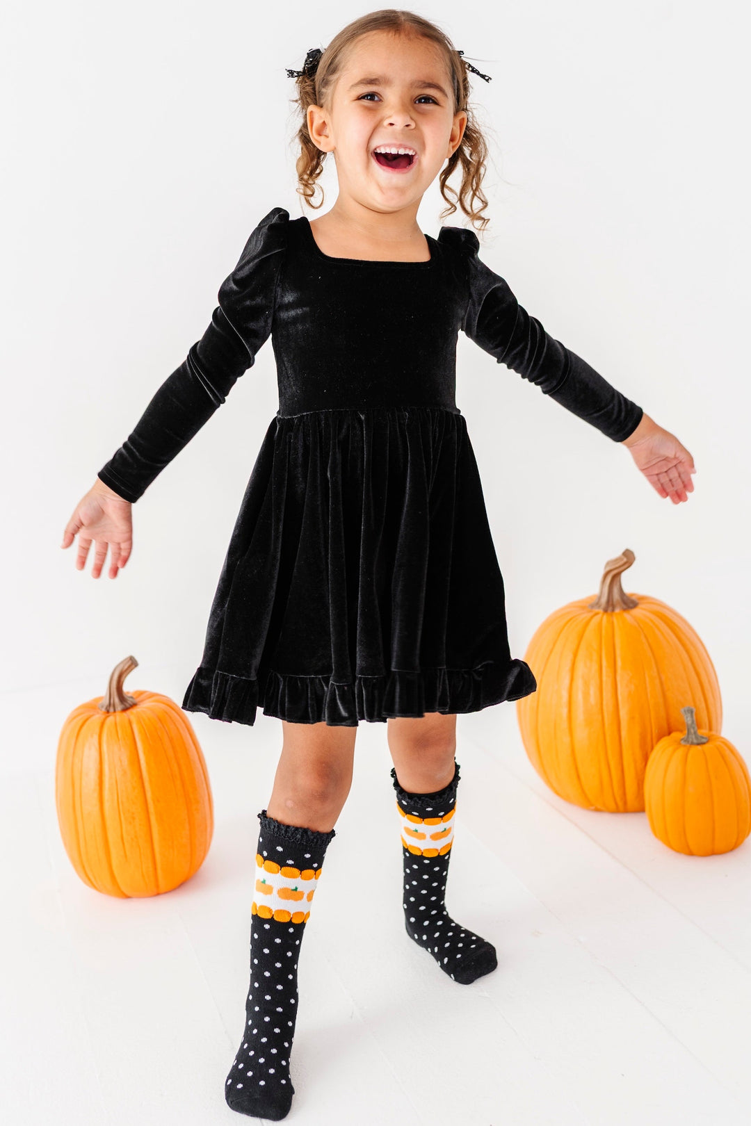 little girl wearing black velvet square neckline dress with pumpkin knee high socks