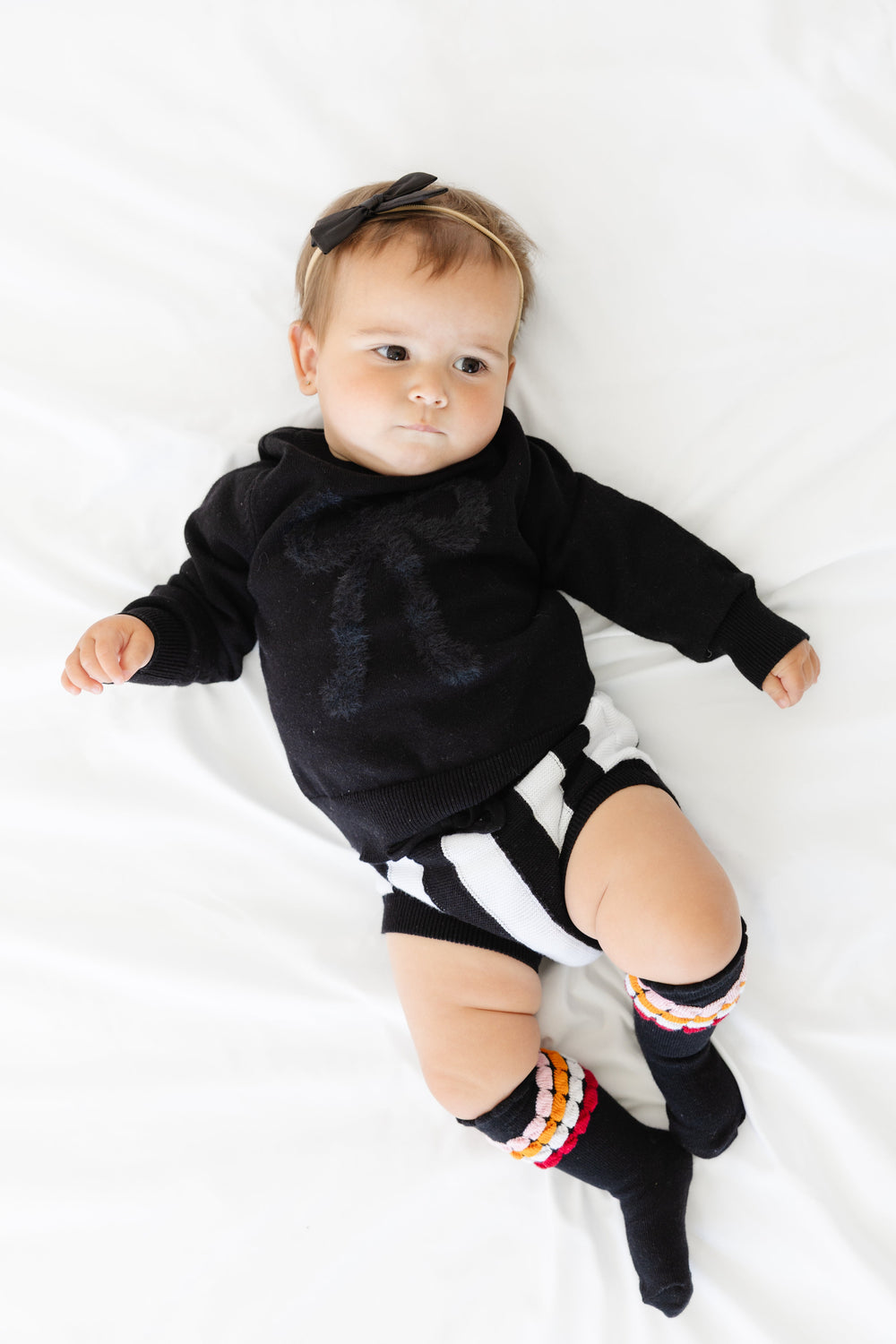 baby girl in black and white striped cotton knit bloomers paired with black pullover sweater with fluffy black bow design, black hairbow and Halloween striped knee high socks
