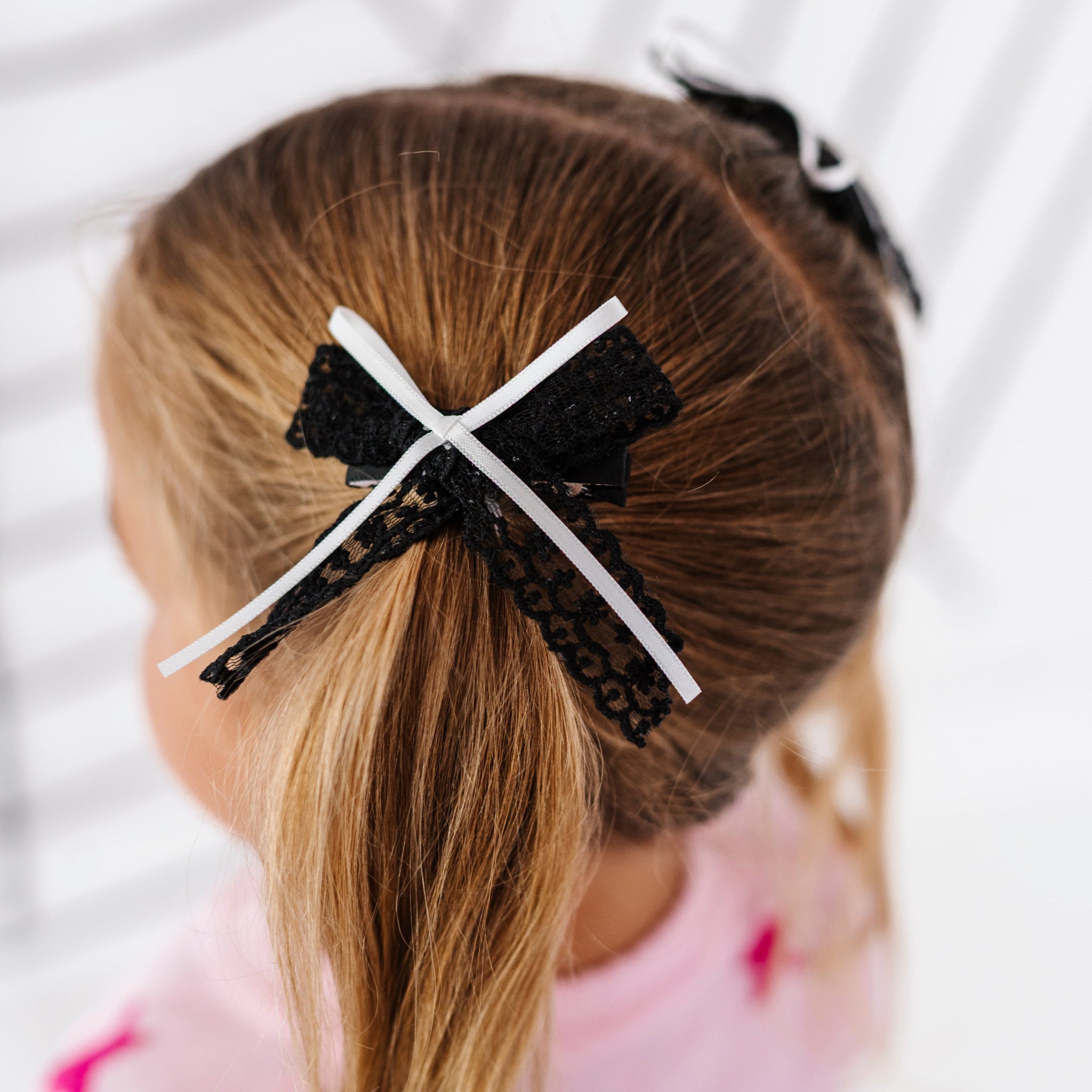little girl in pigtails wearing black lace bows with thin white ribbon embellishment on clips
