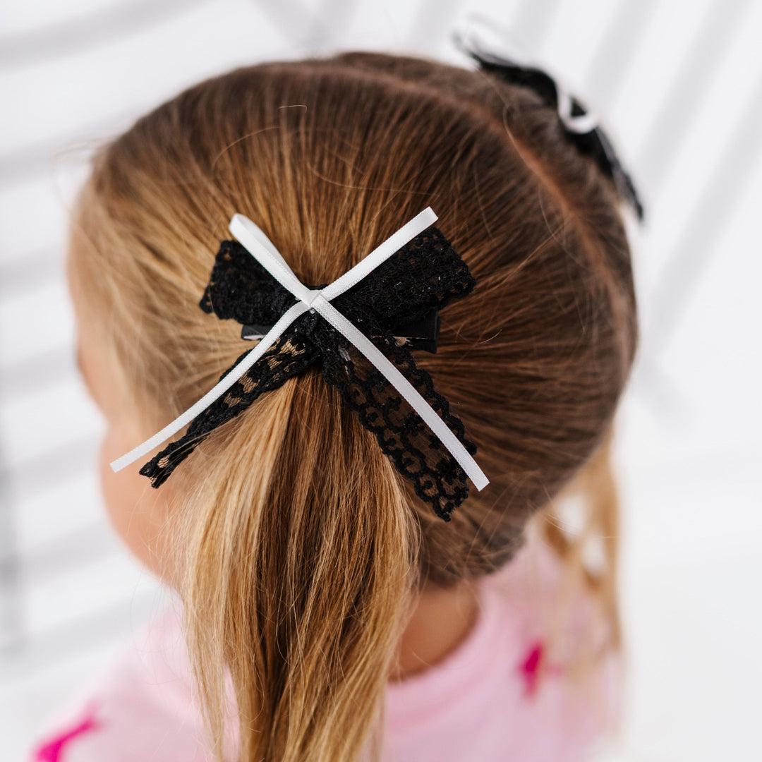 little girl in pigtails wearing black lace bows with thin white ribbon embellishment on clips