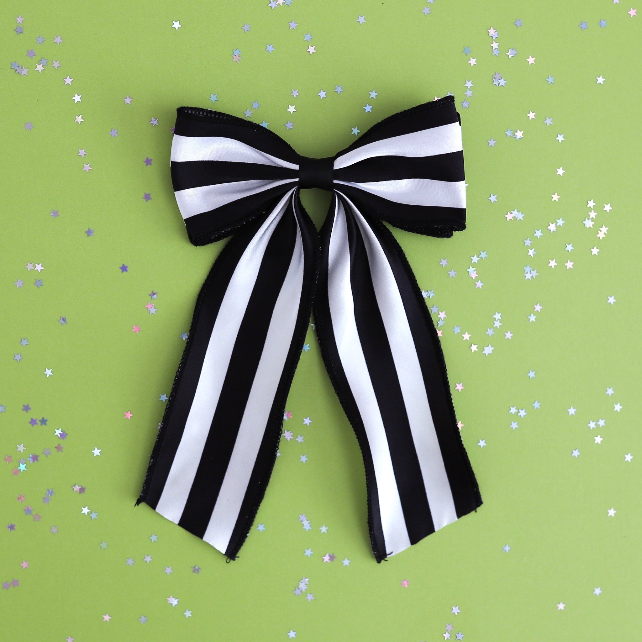 girls wide black and white striped oversized ribbon hair bow on clip photographed on green background with star confetti