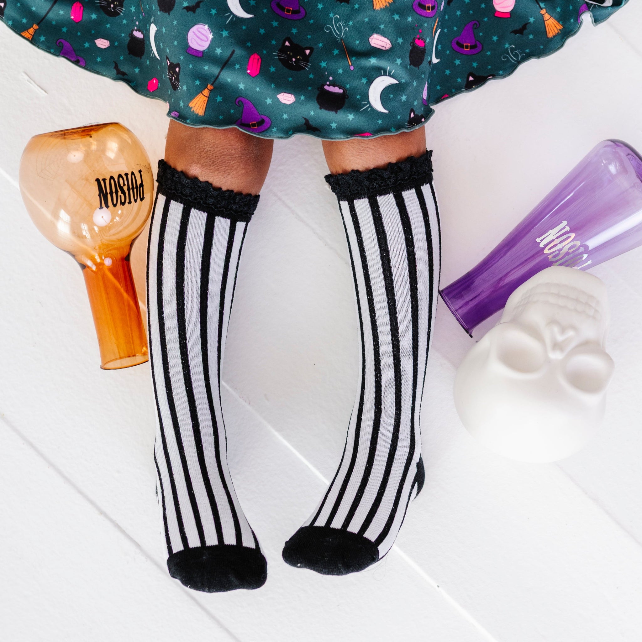 little girl sitting with potion bottles in black and white vertical striped knee socks with lace tops paired with wtitch print twirl dress