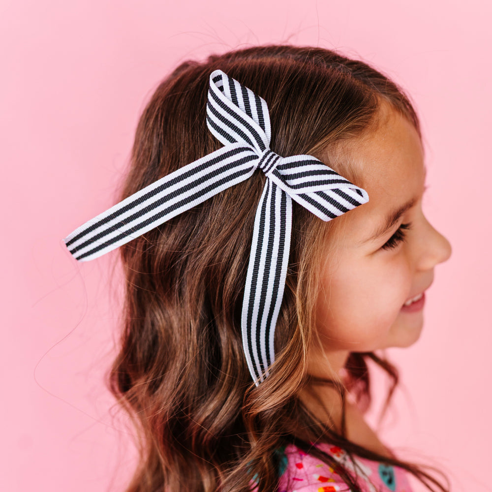 little girl in black and white striped ribbon bow on clip and pink Halloween themed twirl dress
