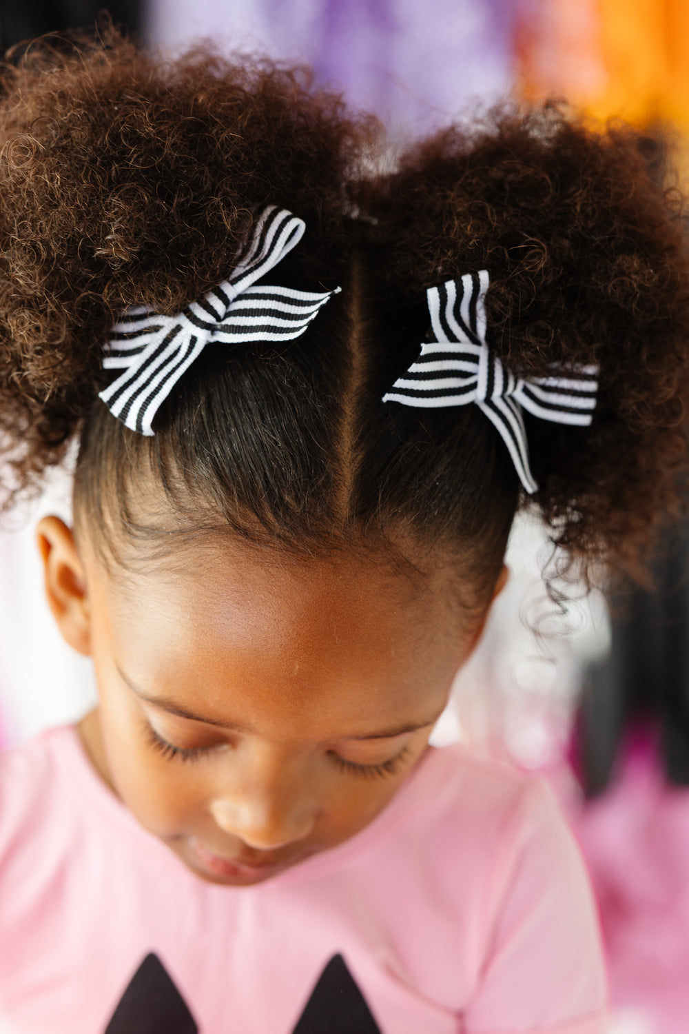 little girl with black and white striped ribbon pigtails bows on clips paired with pink pumpkin tee for Halloween