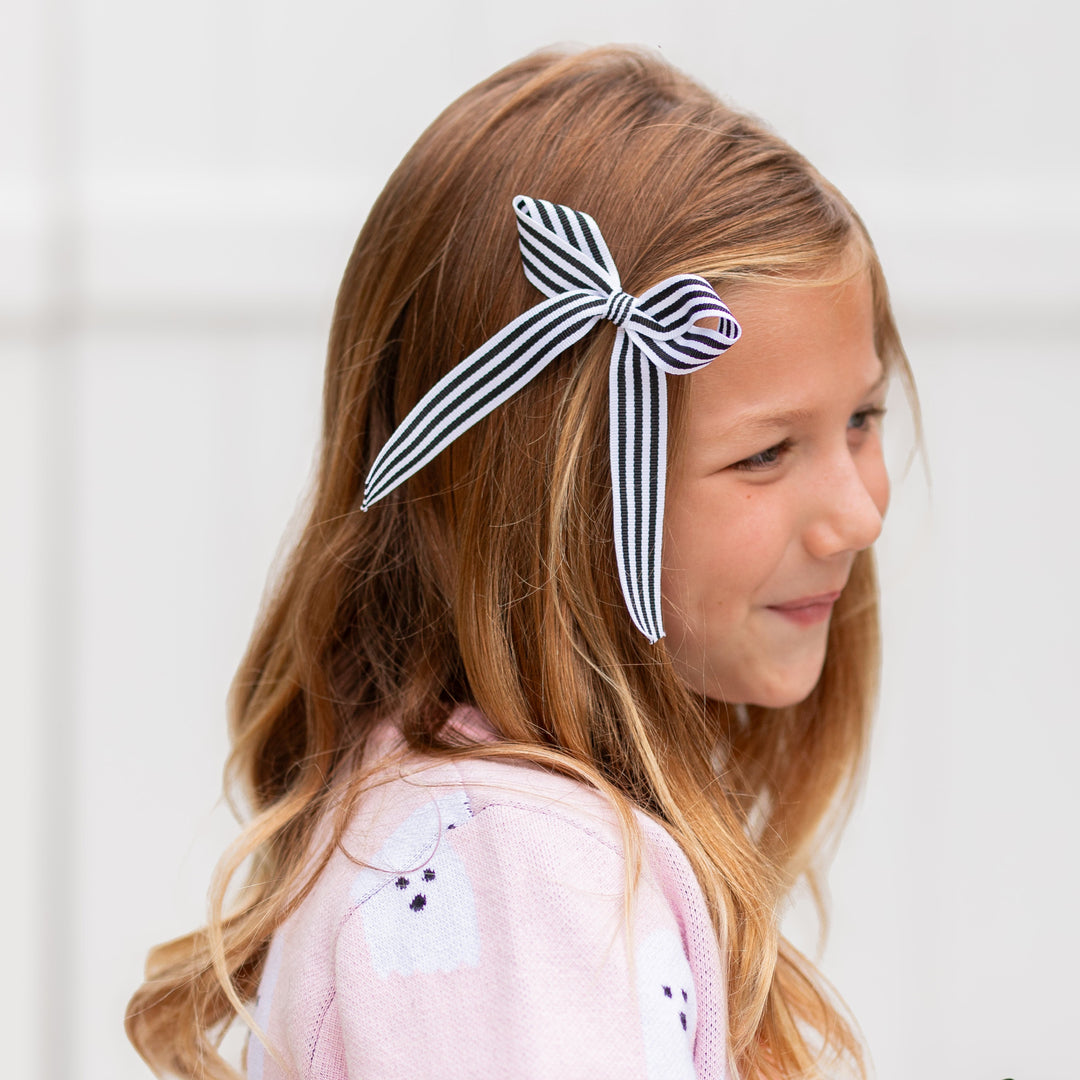 little girl wearing black and white striped ribbon bow on clip and coordinating light pink cardigan with ghost design for Halloween