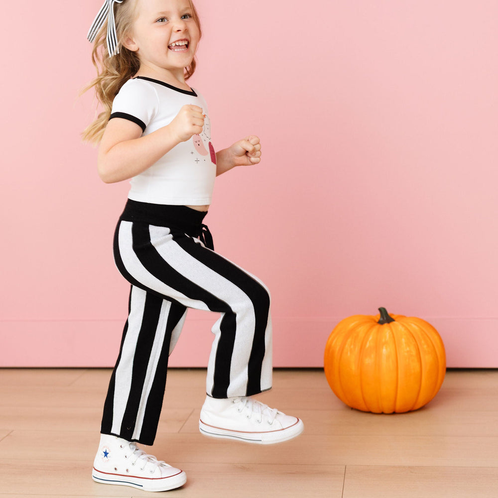 Child in black and white striped pants with a pumpkin on a pink background