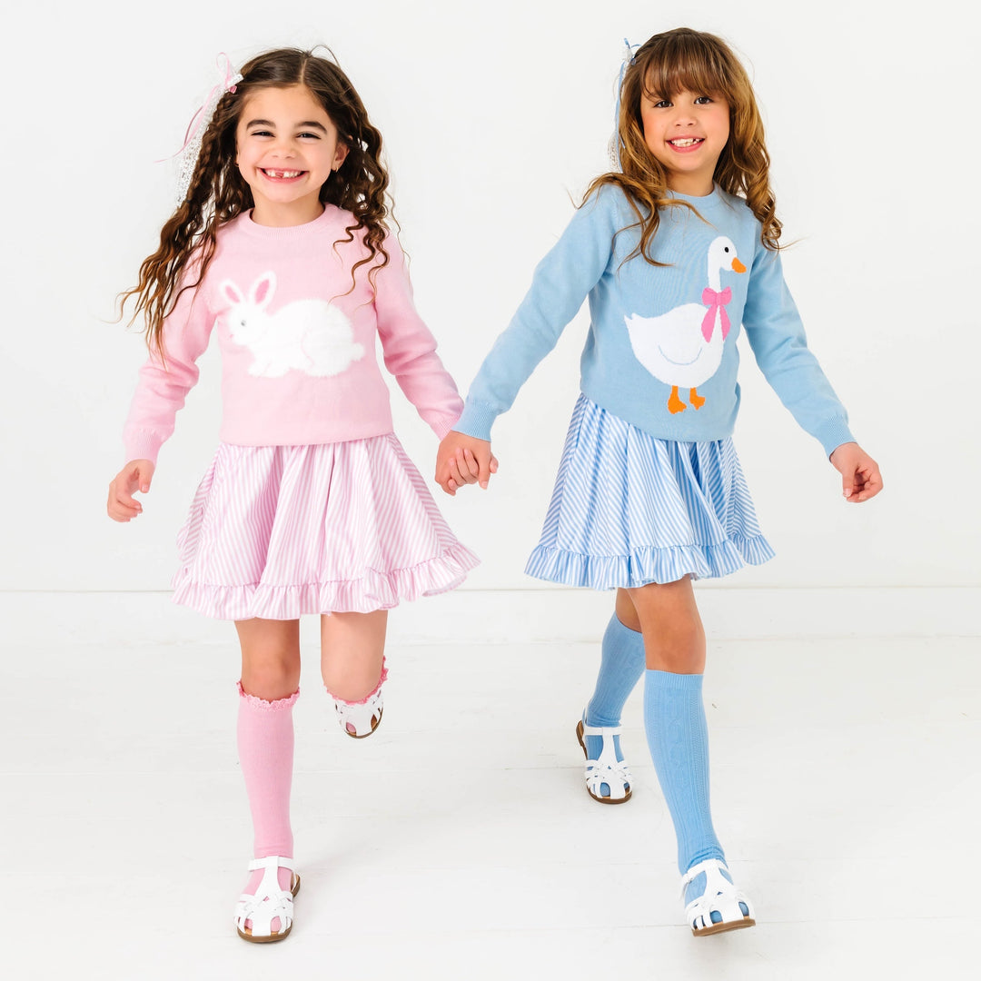 two girls wearing easter outfits with pastel stripes and matching sweaters with a bunny and goose on them
