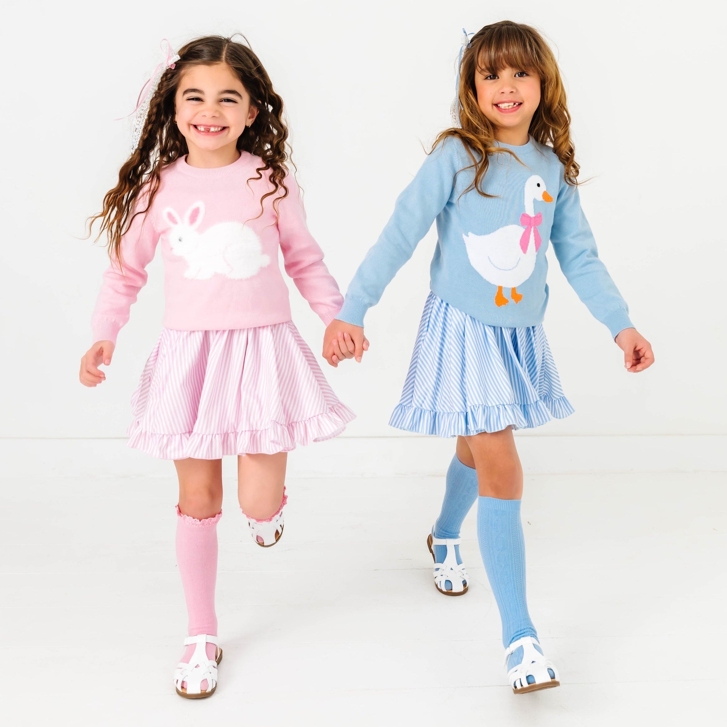 two girls wearing easter outfits with pastel stripes and matching sweaters with a bunny and goose on them
