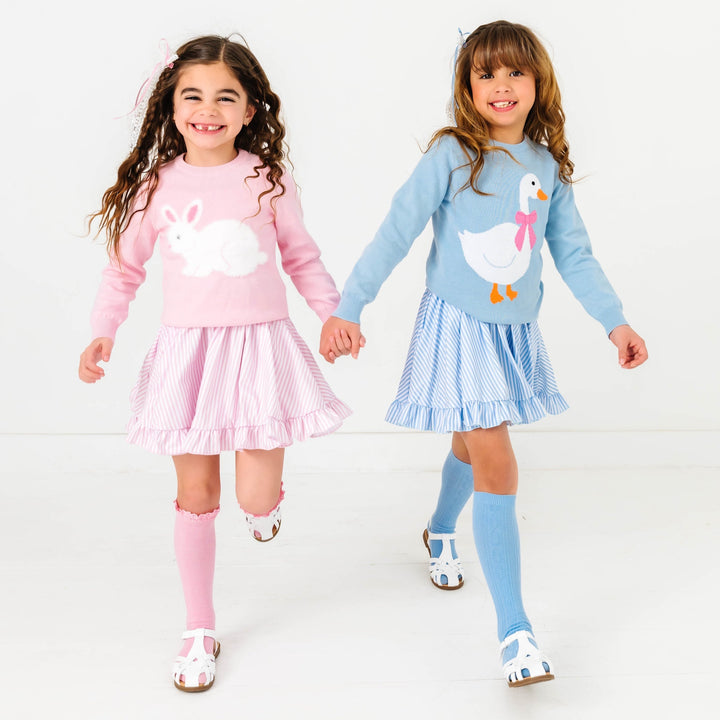 two girls wearing easter outfits with pastel stripes and matching sweaters with a bunny and goose on them