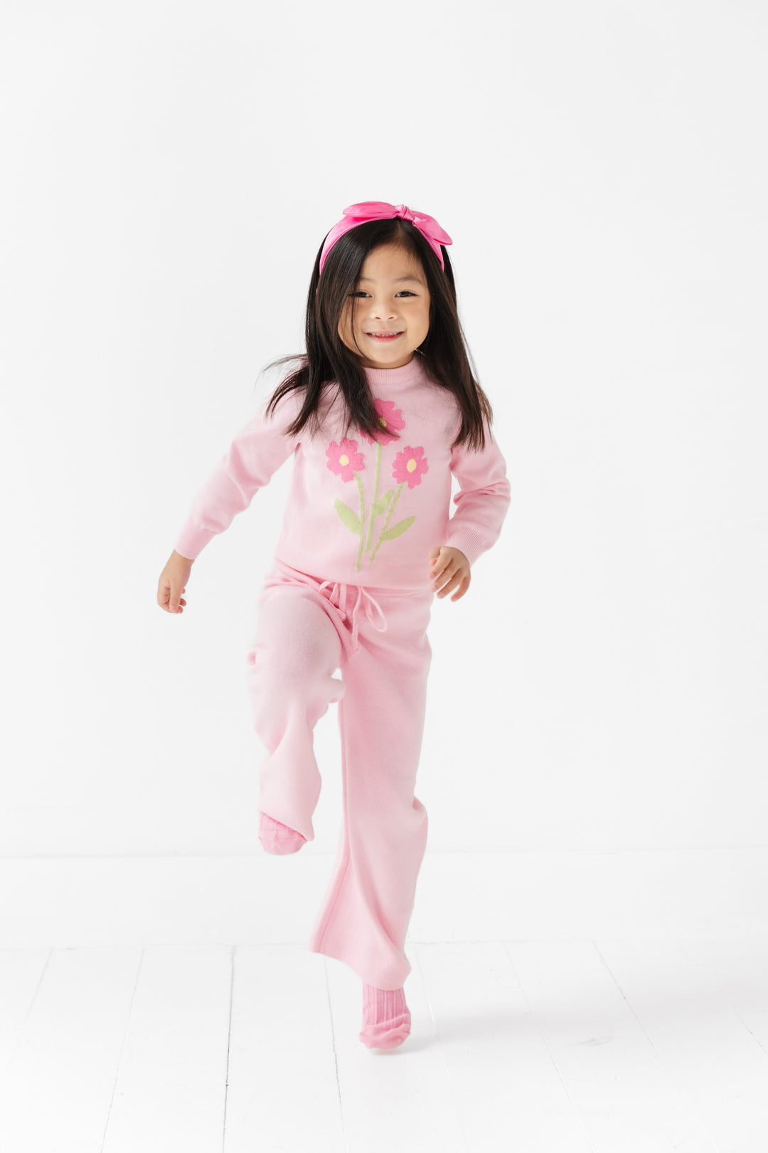 little girl skipping in pastel pink pullover sweater with flower design and matching pink sweater pants and accessories