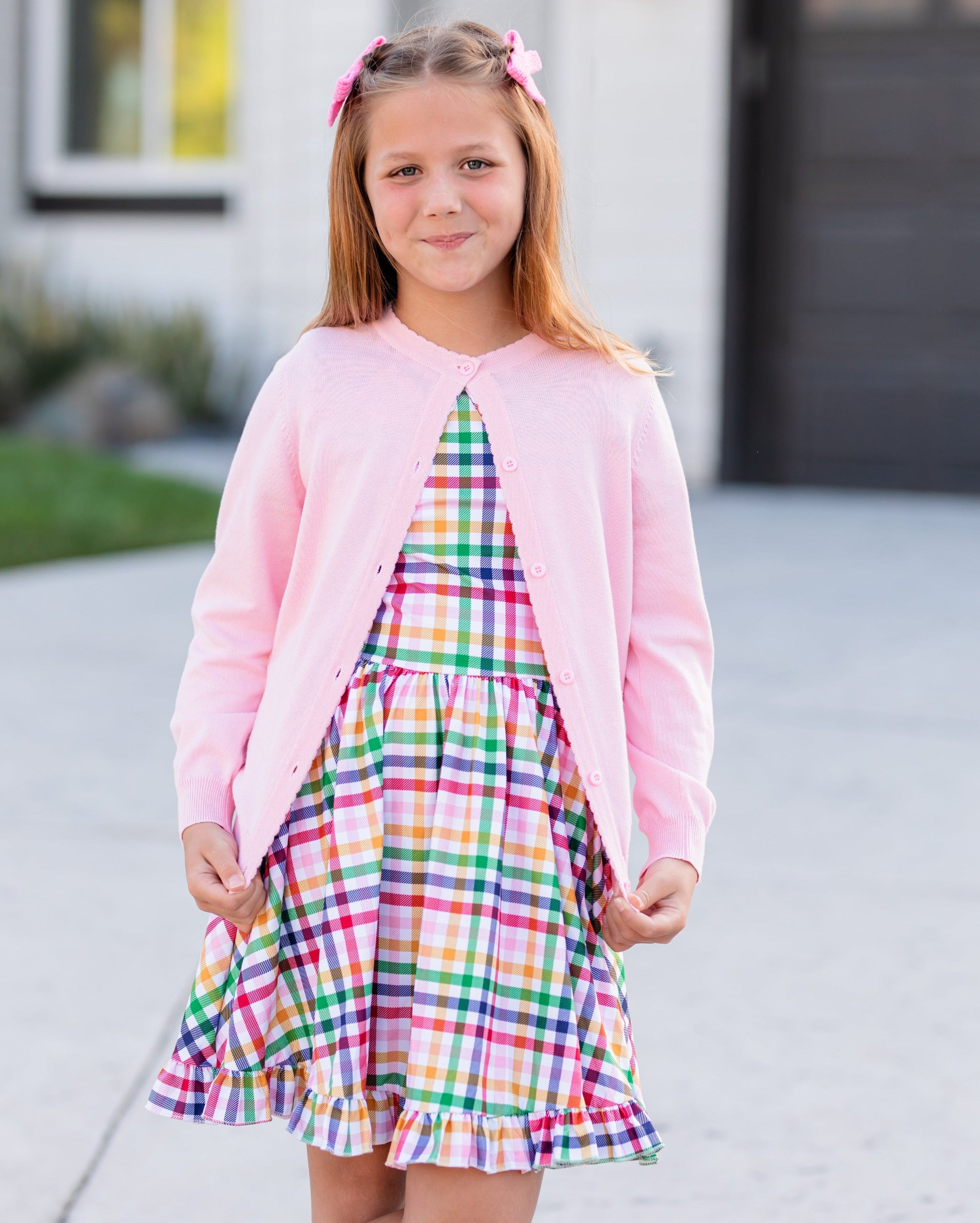 girl posing in back to school outfit with rainbow gingham twirl dress and matching light pink cardigan with scallop trim