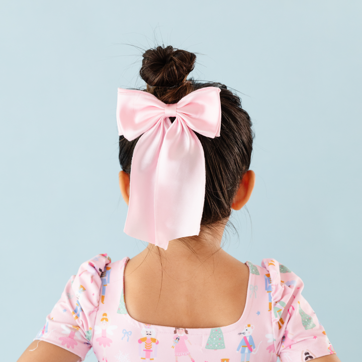 little girl with light pink satin hairbow to match nutcracker themed dress for pastel Christmas vibes