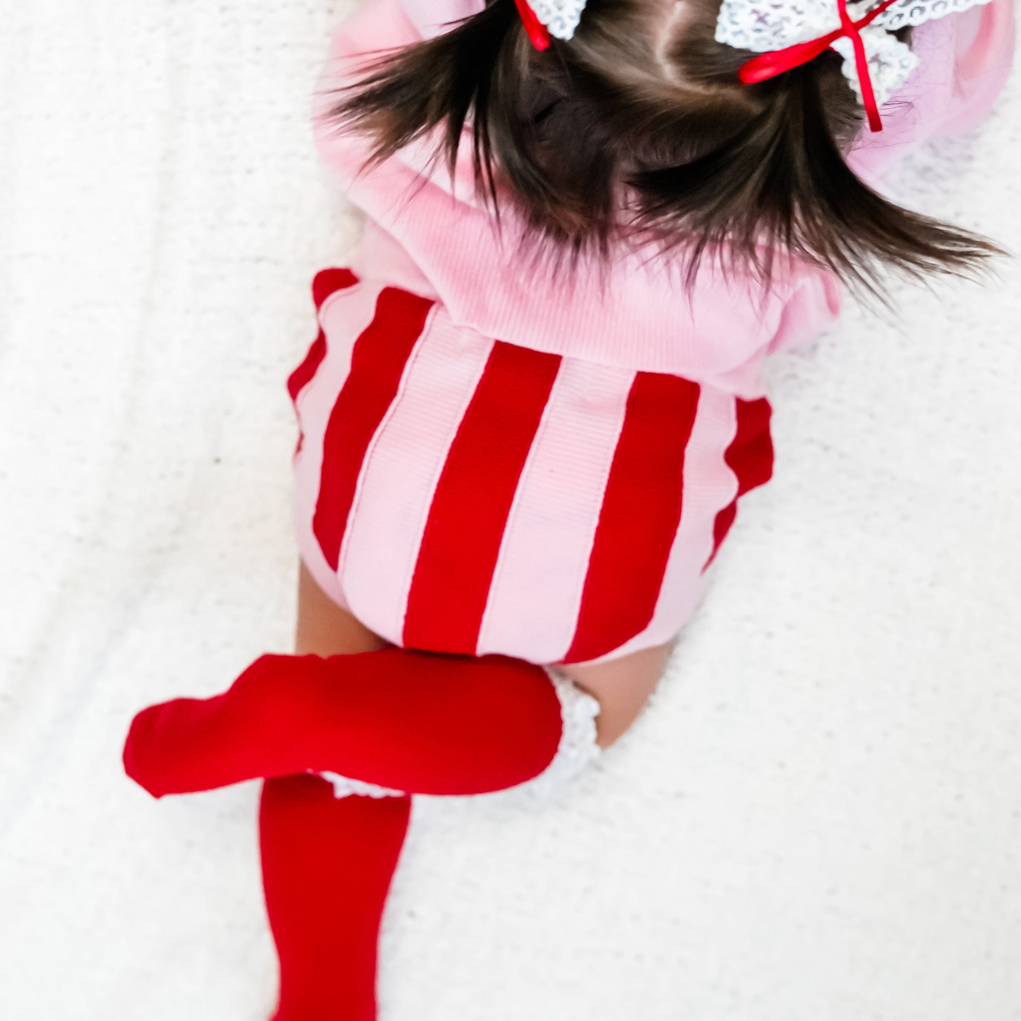 closeup of baby girl in red and pink striped sweater bloomers and red knee high socks with white lace