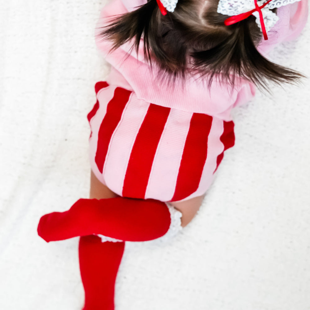 closeup of baby girl in red and pink striped sweater bloomers and red knee high socks with white lace