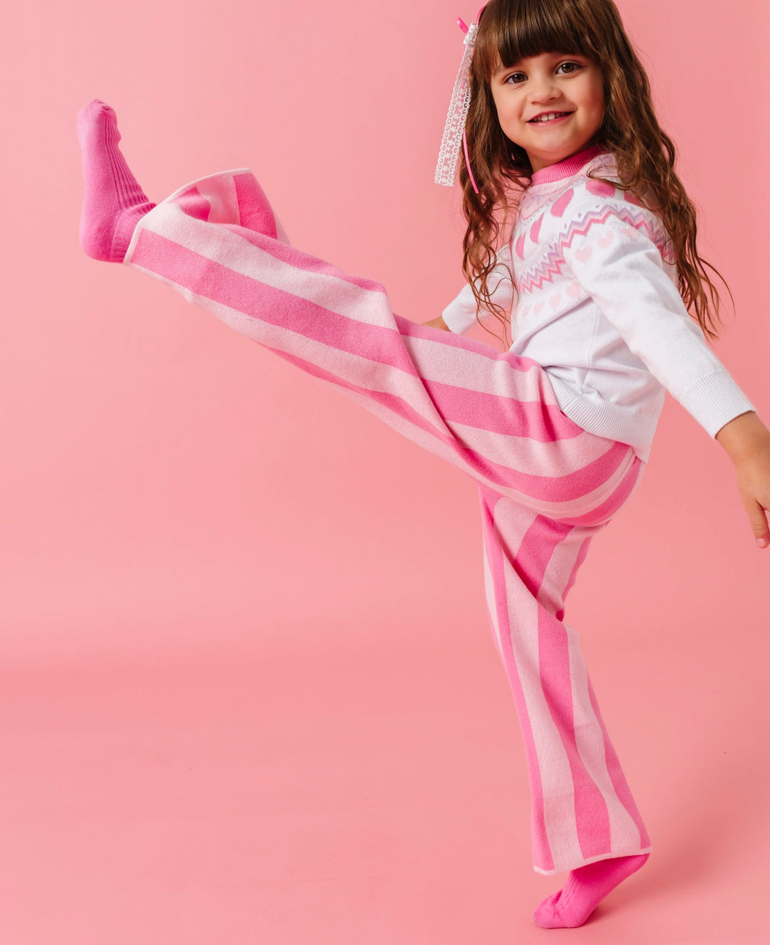 little girl high kicking in two-tone pink striped sweater pants, pink socks and white fair isle sweater with a valentine's theme