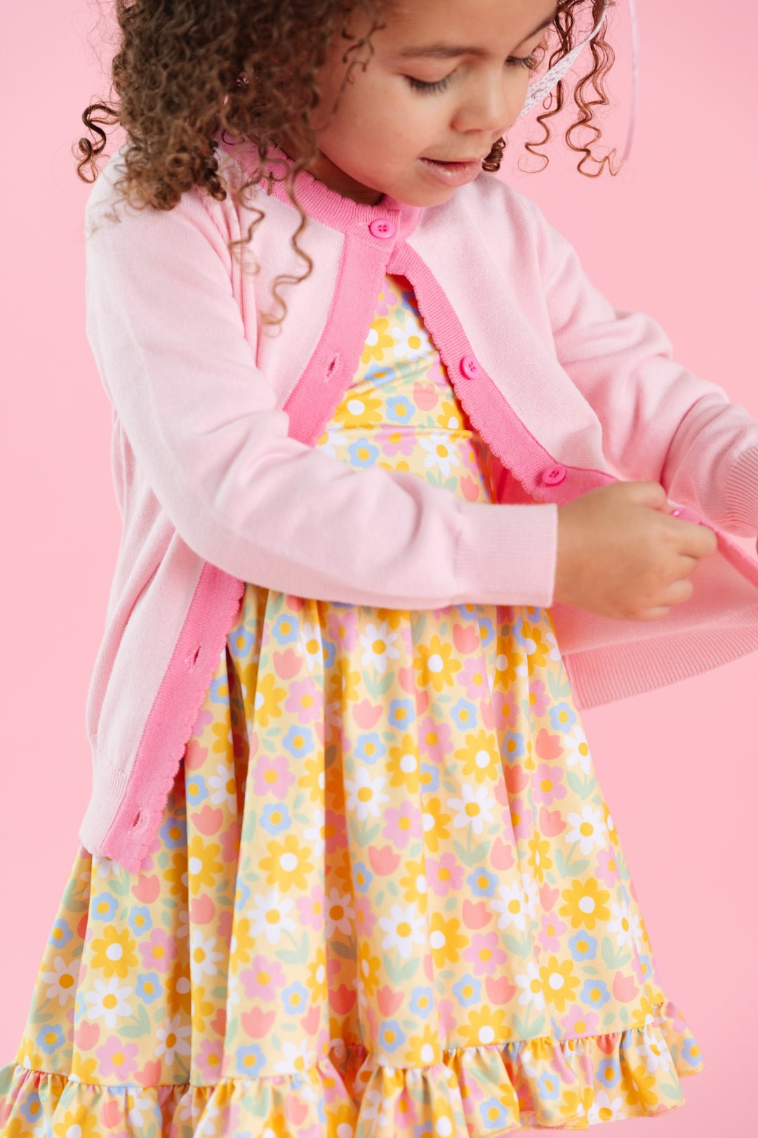 girl in light pink cardigan with contrasting taffy pink scallop trim and matching spring yellow floral dress