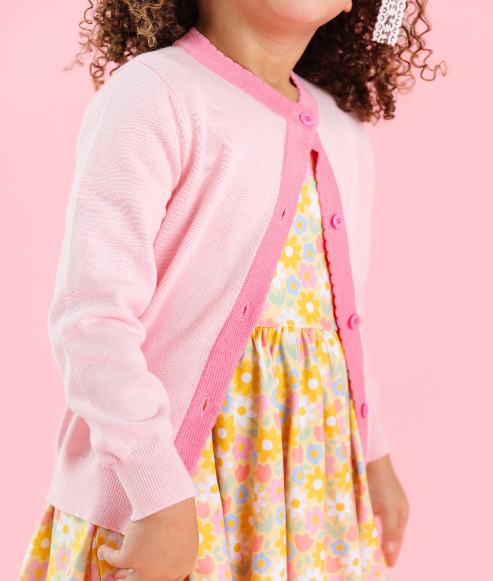 girl in light pink cardigan with contrasting taffy pink scallop trim and matching spring yellow floral dress