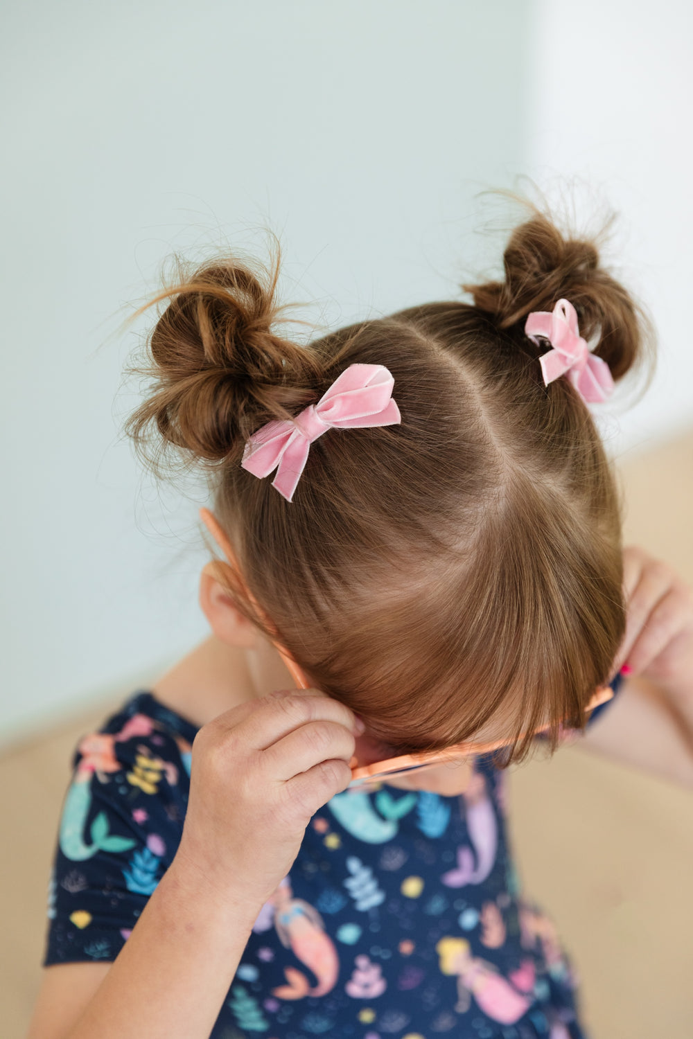 little girl with pigtail buns styled with light pink velvet ribbon pigtail bows on clips and mermaid print twirl dress