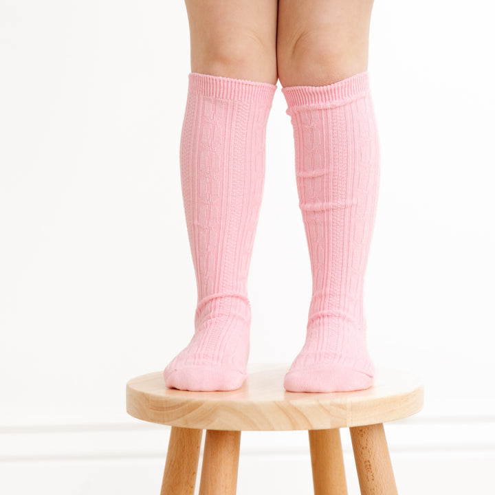 little girl standing on wooden stool wearing blossom pink cable knit knee high socks
