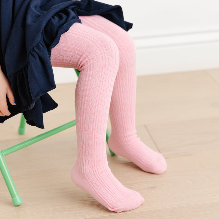 little girl sitting on chair in navy twirl dress wearing light blossom pink cable knit tights