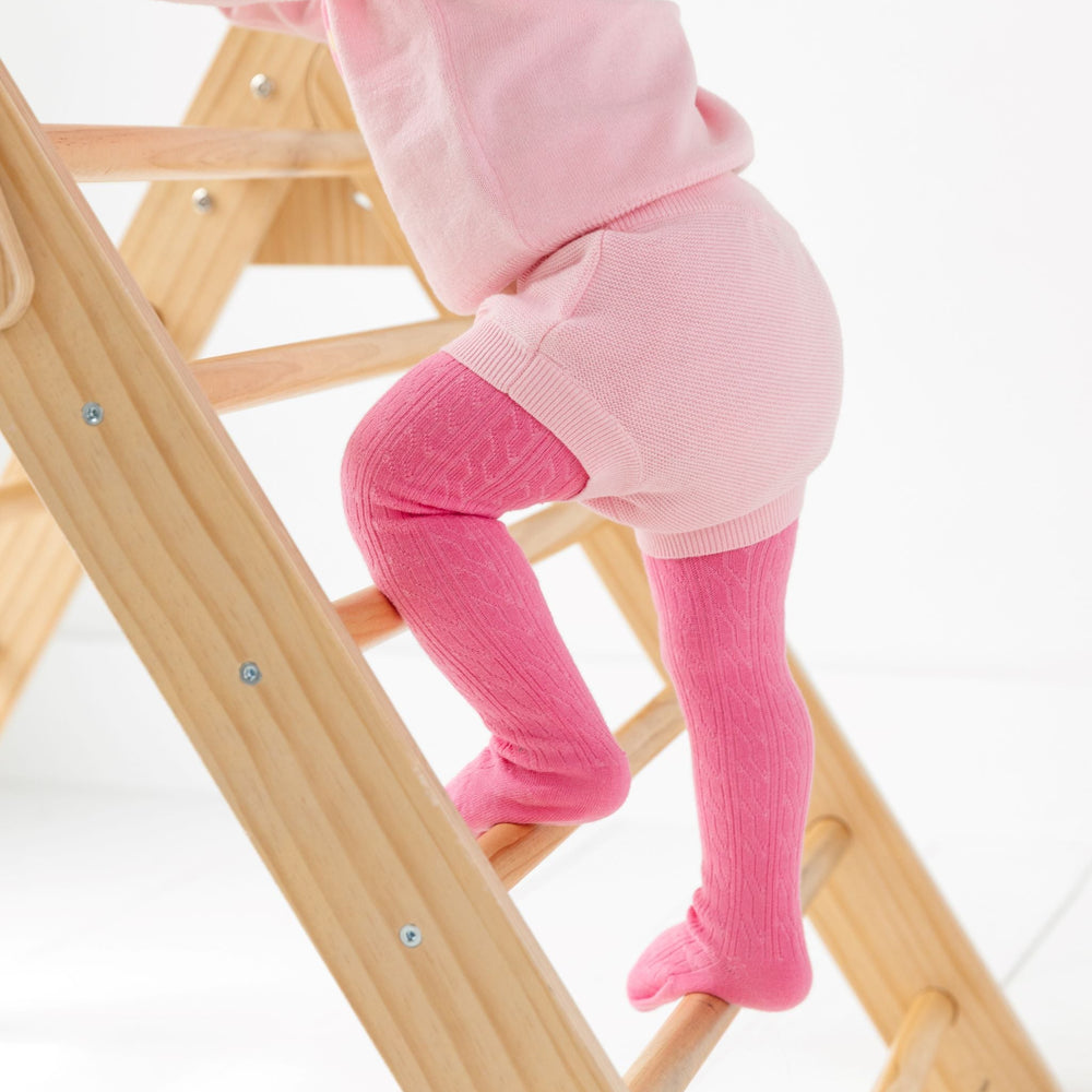 baby girl climbing pikler in pastel pink cotton knit bloomers paired with matching pink pullover sweater and taffy pink cable knit tights for spring