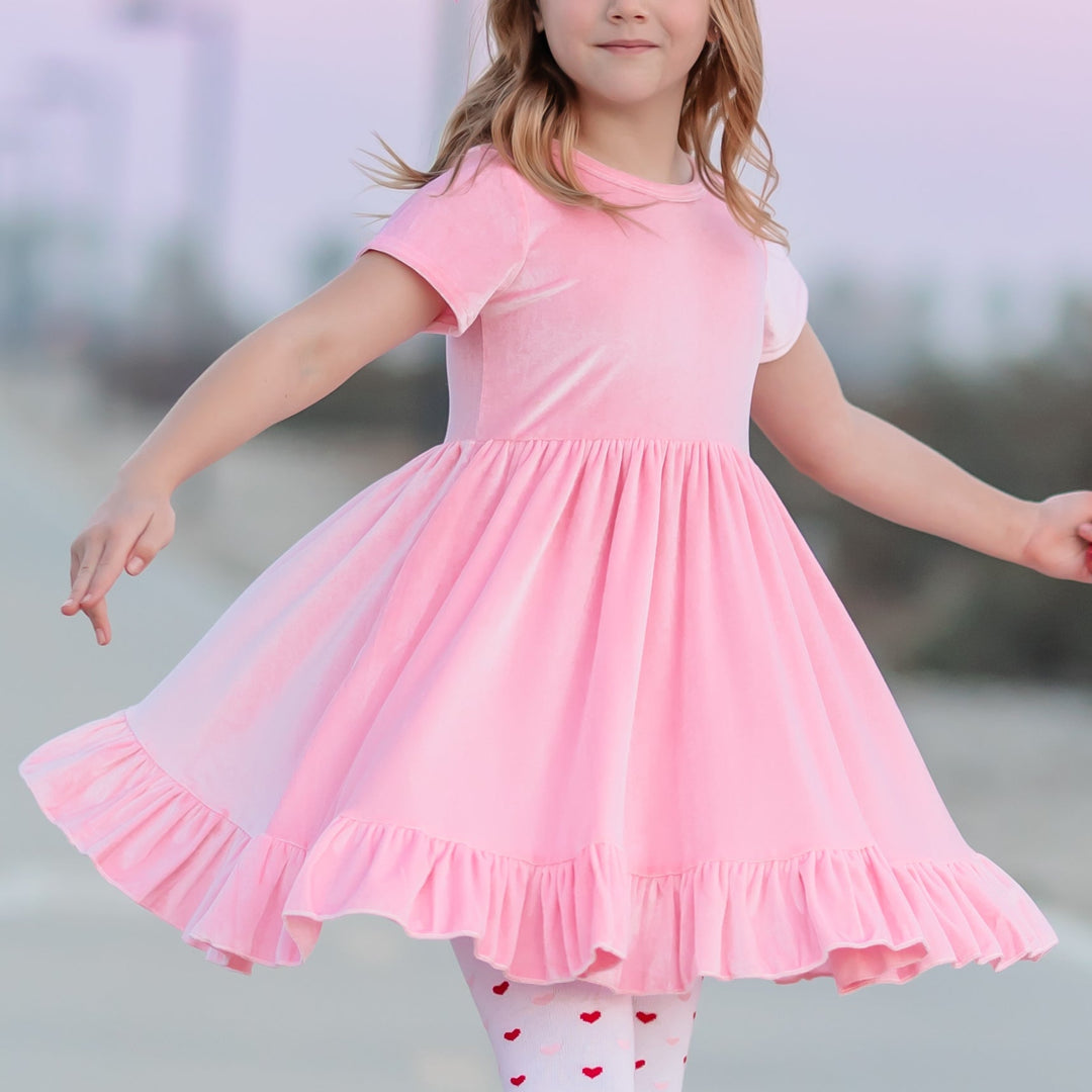 little girl twirling in pastel pink velvet dress with ruffle hem and matching Valentine's Day heart tights