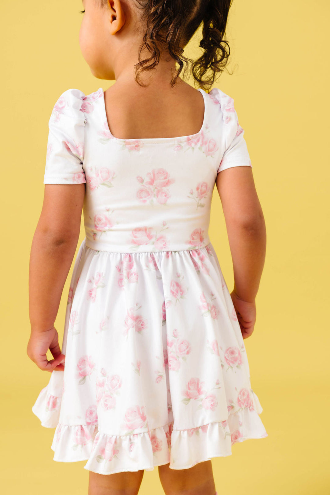 back view of little girl in square neck twirl dress with pastel pink roses on white background