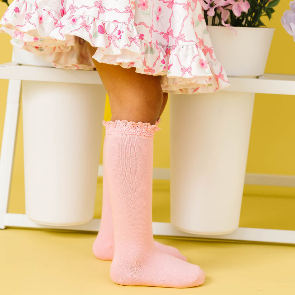 Child wearing a floral dress and pink  lace trim knee high socks on a yellow background