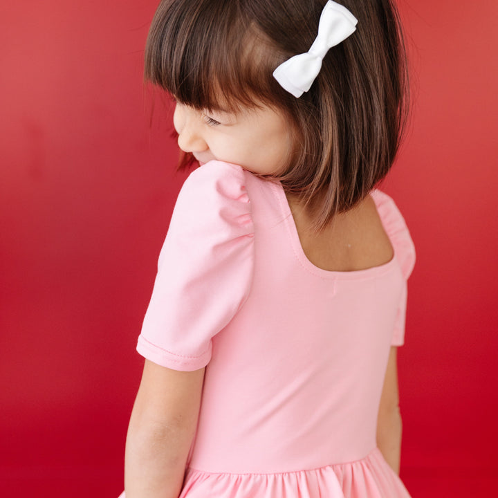 closeup of puff sleeve and square neckline on little girl's light pink twirl dress with matching white satin bow