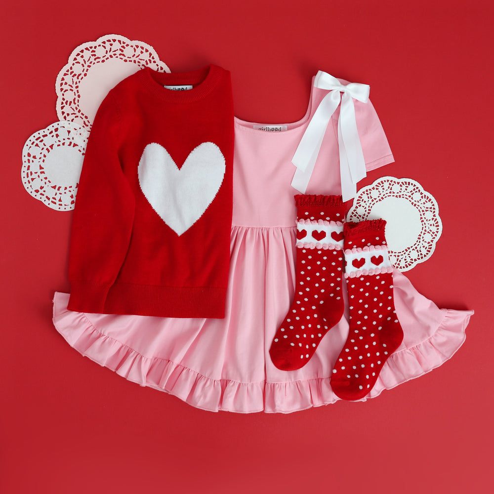 little girls styled Valentines outfit with light pink cotton twirl dress, red pullover heart sweater, white satin bow and matching red dot and heart knee high socks